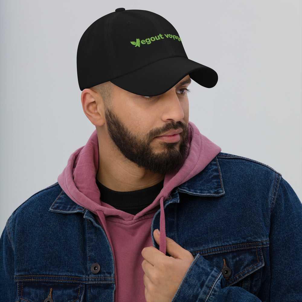 Man wearing a black cap with green text, pink hoodie, and blue jacket on a gray background