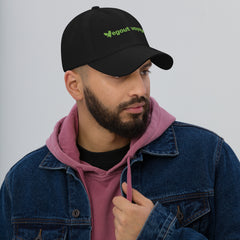 Man wearing a black cap with green text, pink hoodie, and blue jacket on a gray background