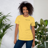 Smiling woman wearing yellow Vegout Voyage t-shirt standing by indoor plants