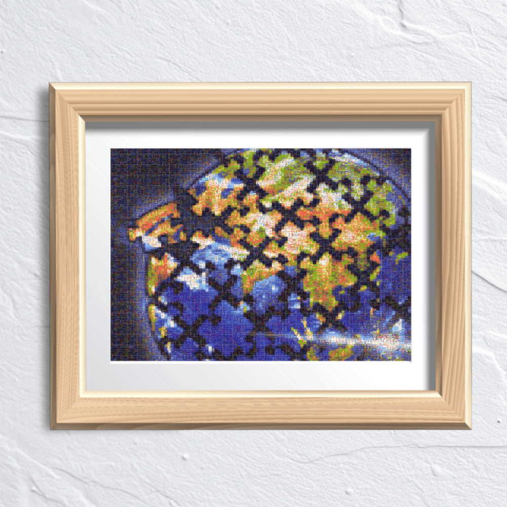 A framed art print featuring a pixelated globe with a black puzzle-piece overlay pattern, set in a light wood frame with a white mat against a textured white wall.