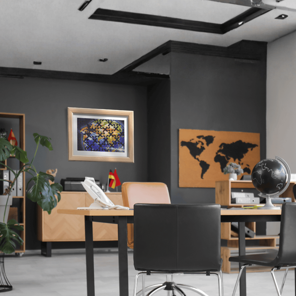 A modern office interior with a dark gray wall, a framed colorful stained-glass-style artwork, a world map poster, a desk, chairs, shelving, and office decor.