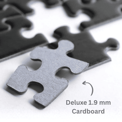 Close-up of metal jigsaw puzzle pieces on a white surface, with one front piece in sharp focus and blurred pieces behind it. Text reads 'Deluxe 1.