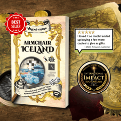 Book cover for 'Armchair Iceland' displayed on a wooden surface with vintage map and coin props. The cover features ornate gold detailing, a magnifying glass over an icy landscape illustration, and text including 'A Puzzle Game-inspired Travel Adventure Book for Grown-Ups.