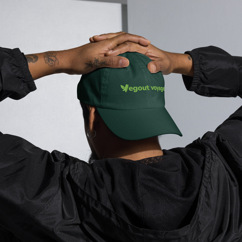 Person holding a green cap with 'Vegout Voyages' logo against a neutral background