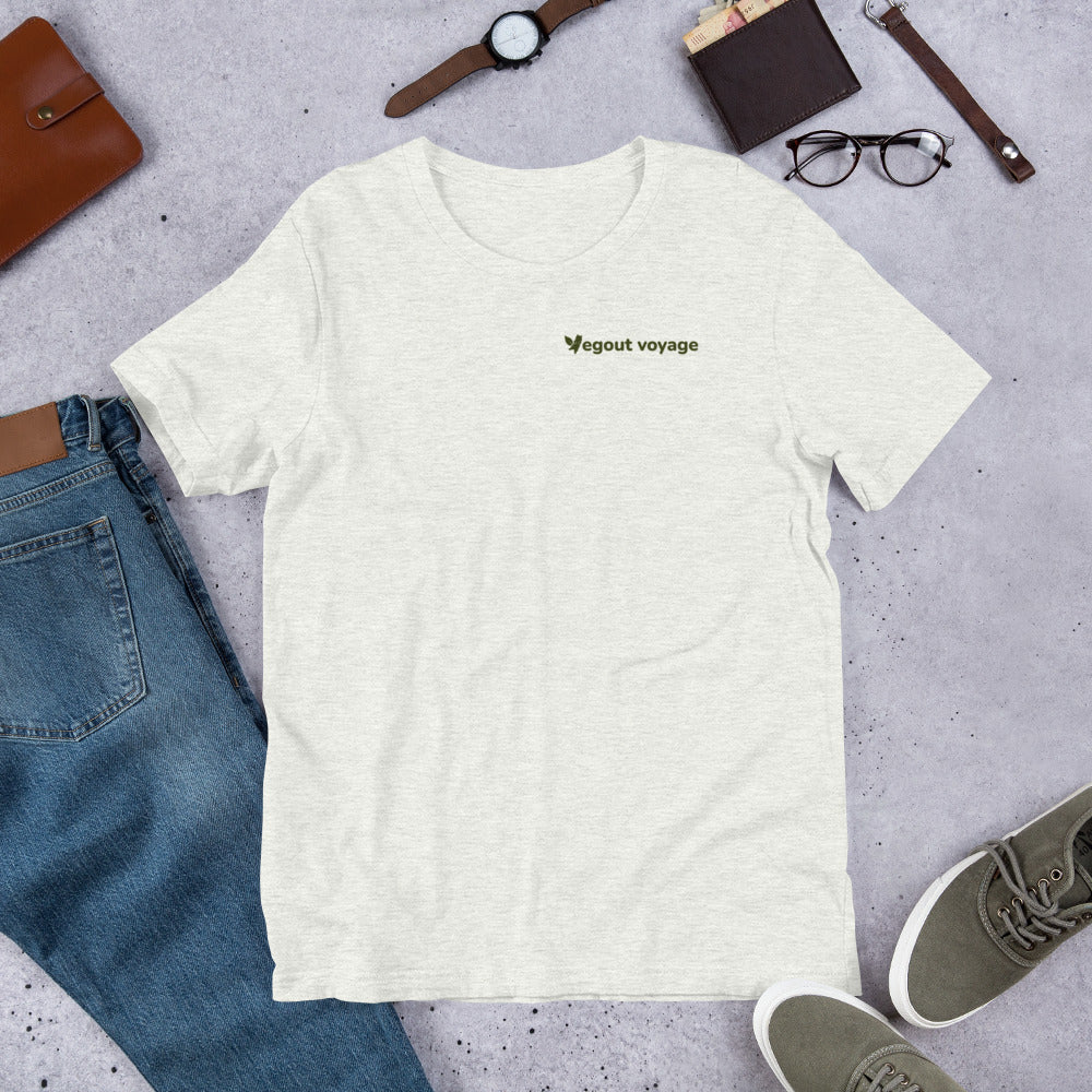 Flat lay of an ash-colored "Vegout Voyage" logo t-shirt paired with jeans, accessories, and casual shoes