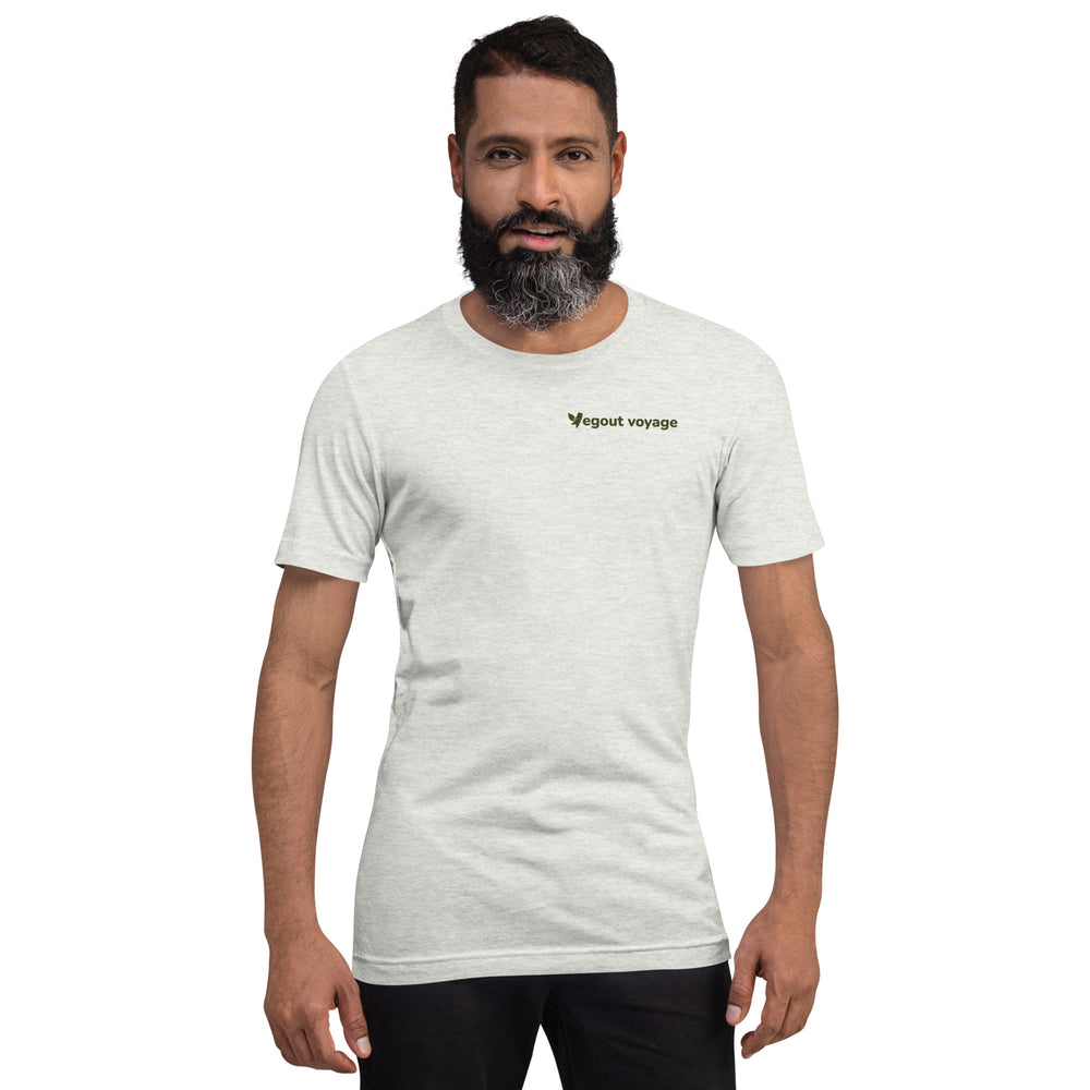 Bearded man wearing an ash-colored "Vegout Voyage" t-shirt, standing confidently with arms relaxed.