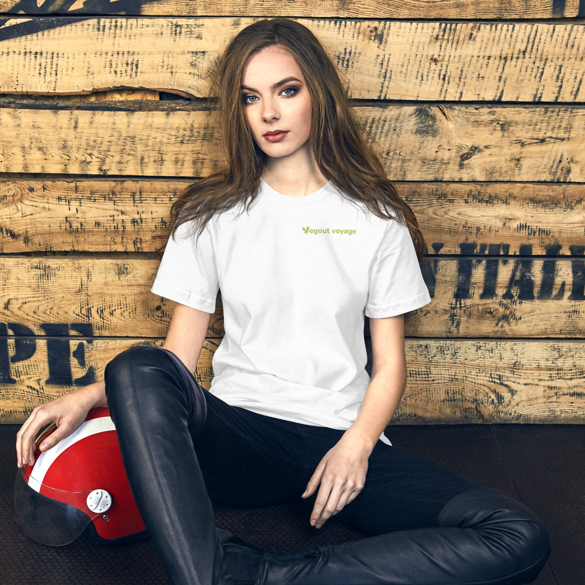 Woman wearing Vegout Voyage logo t-shirt in white while sitting against wooden backdrop